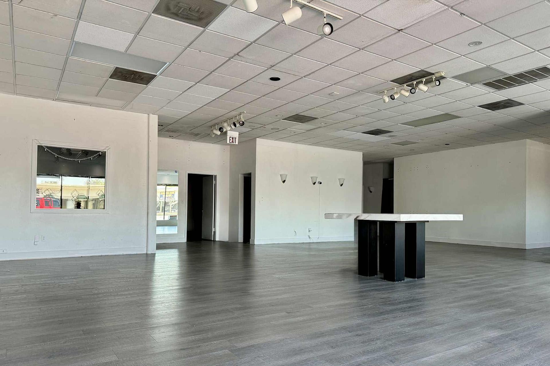 Empty white commercial space with gray flooring, track lighting, and a black and white display table.