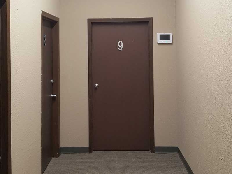 A hallway with two brown doors and a thermostat on the wall.