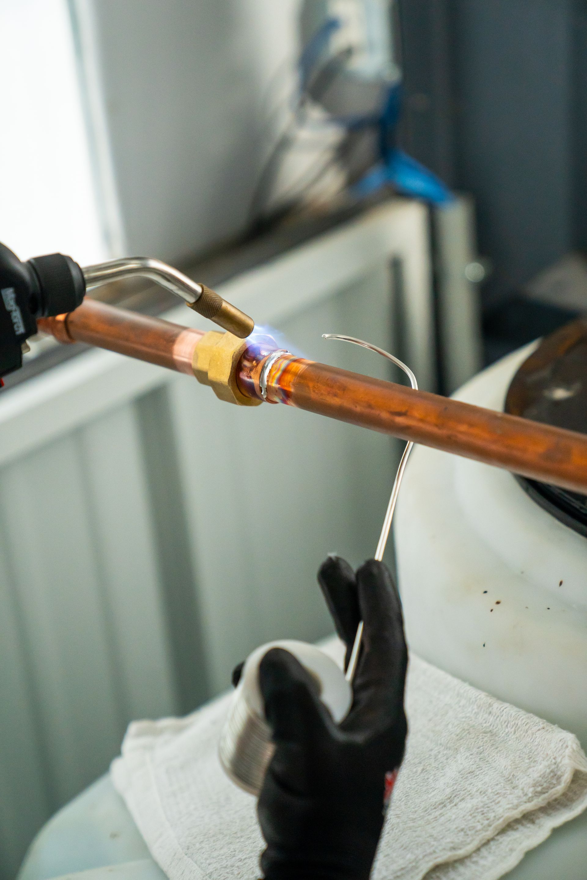 Person brazing copper pipe with a torch, wearing gloves.