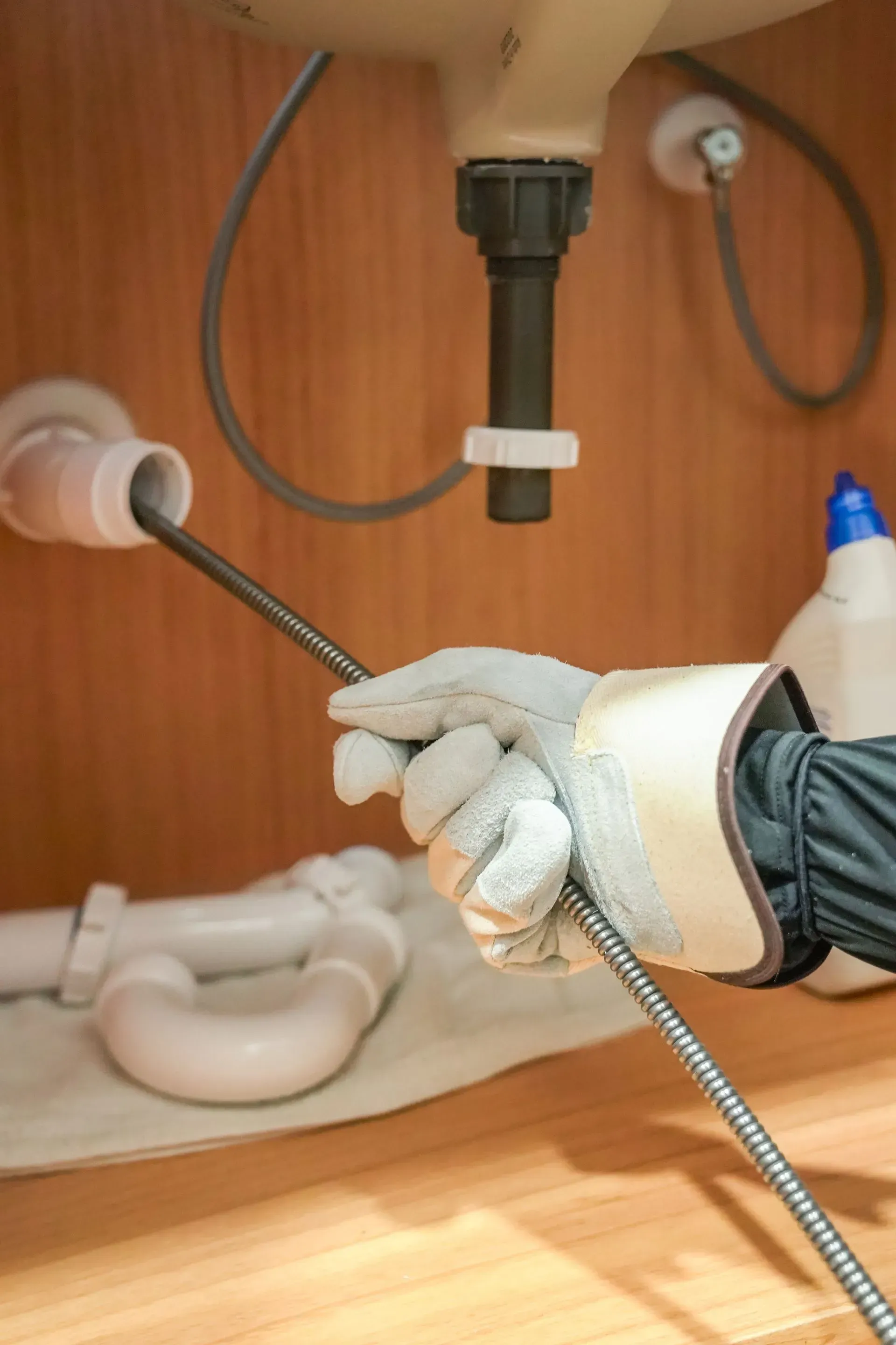 Hand in work glove using snake tool to unclog sink drain.