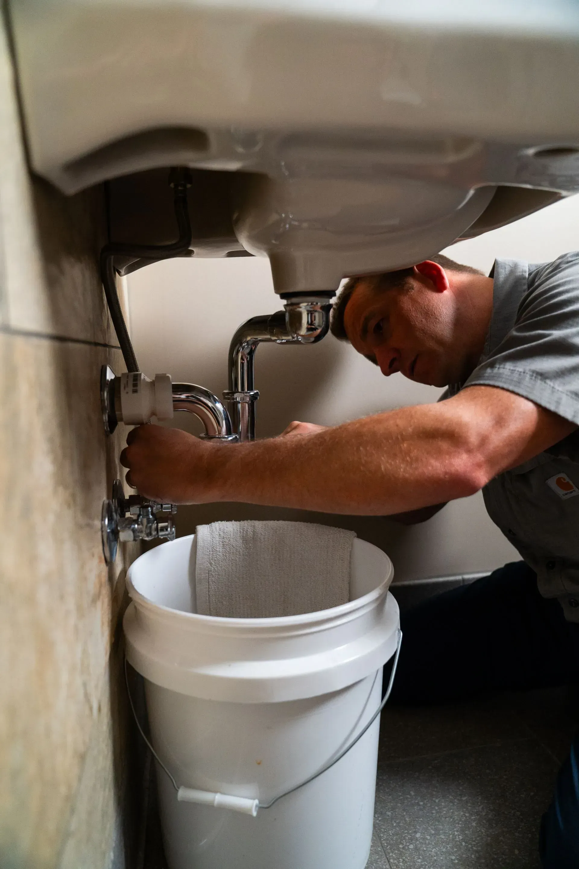 Plumber working under a sink, using a bucket to catch water.