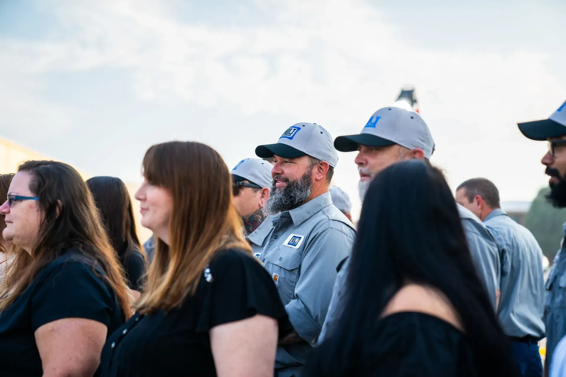 Group of people in hats and work shirts looking towards the right side of the frame.