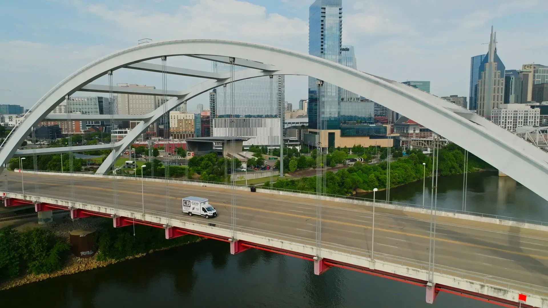 White van crossing a bridge in Nashville, TN, with city skyline in the background.