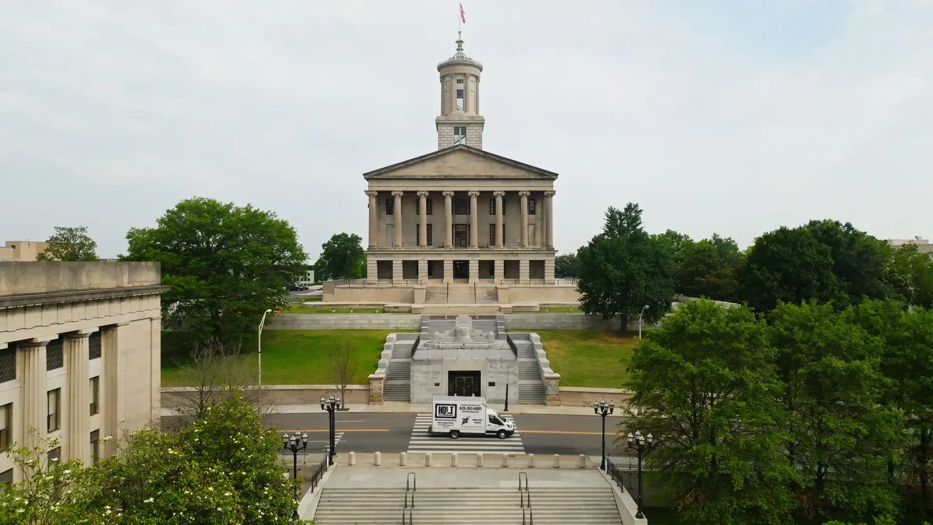 Tennessee State Capitol building with a white vehicle on the road and trees in the foreground.