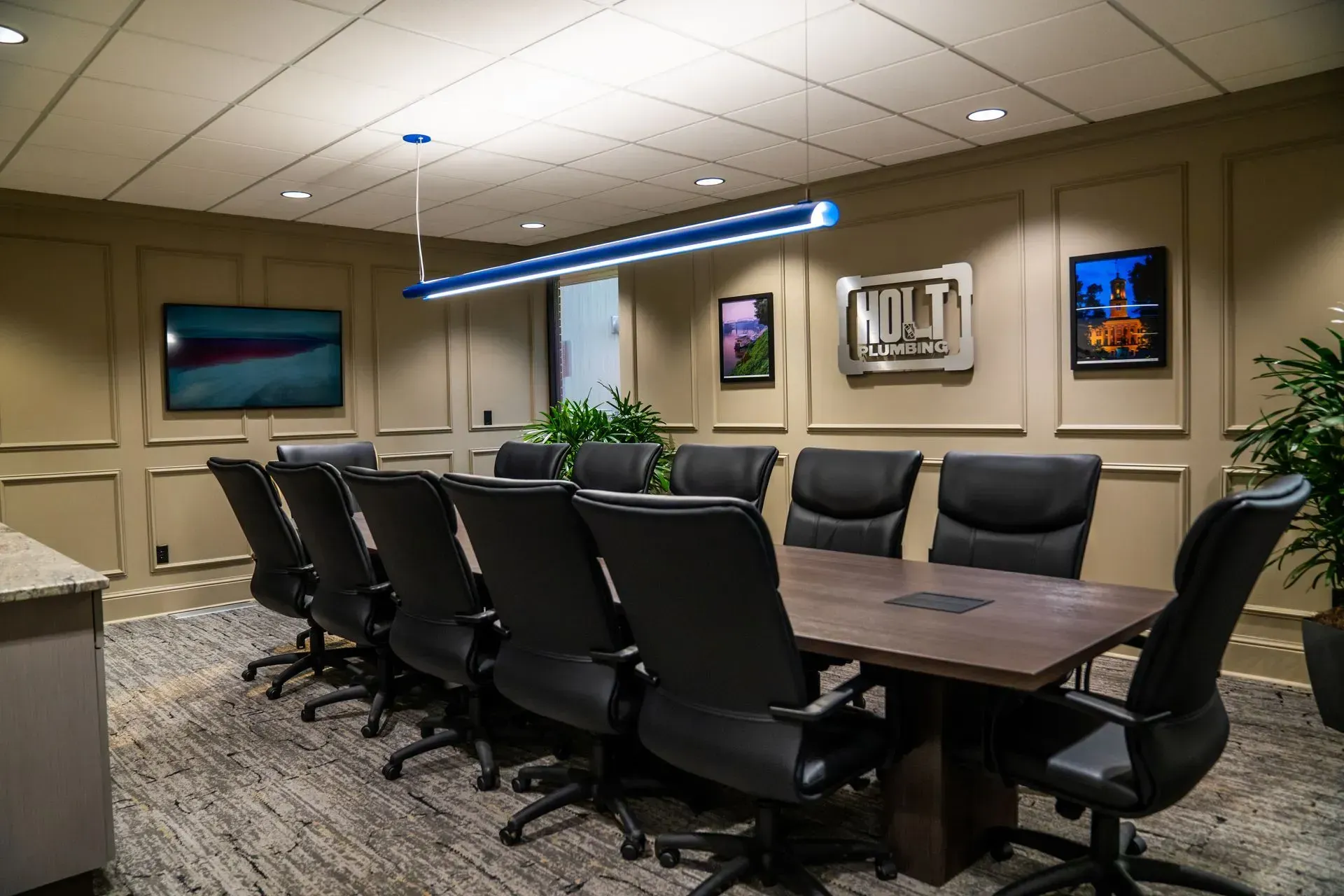 Conference room with long table, black chairs, artwork, and modern light fixture.