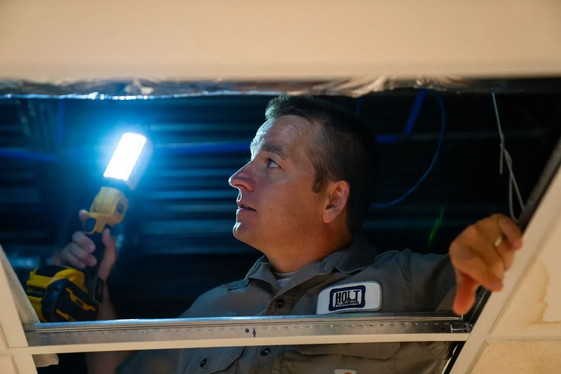 Man with flashlight inspecting ceiling opening.