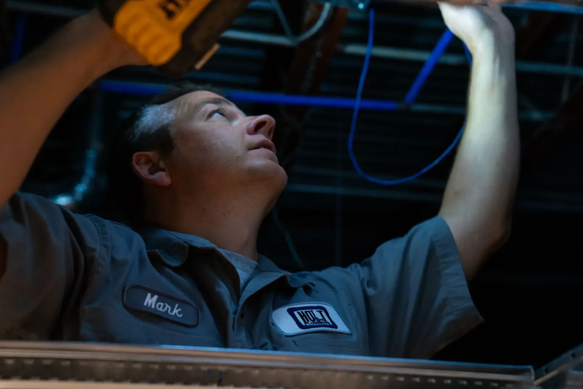 Man in work uniform, using a flashlight to work on wiring in a ceiling.