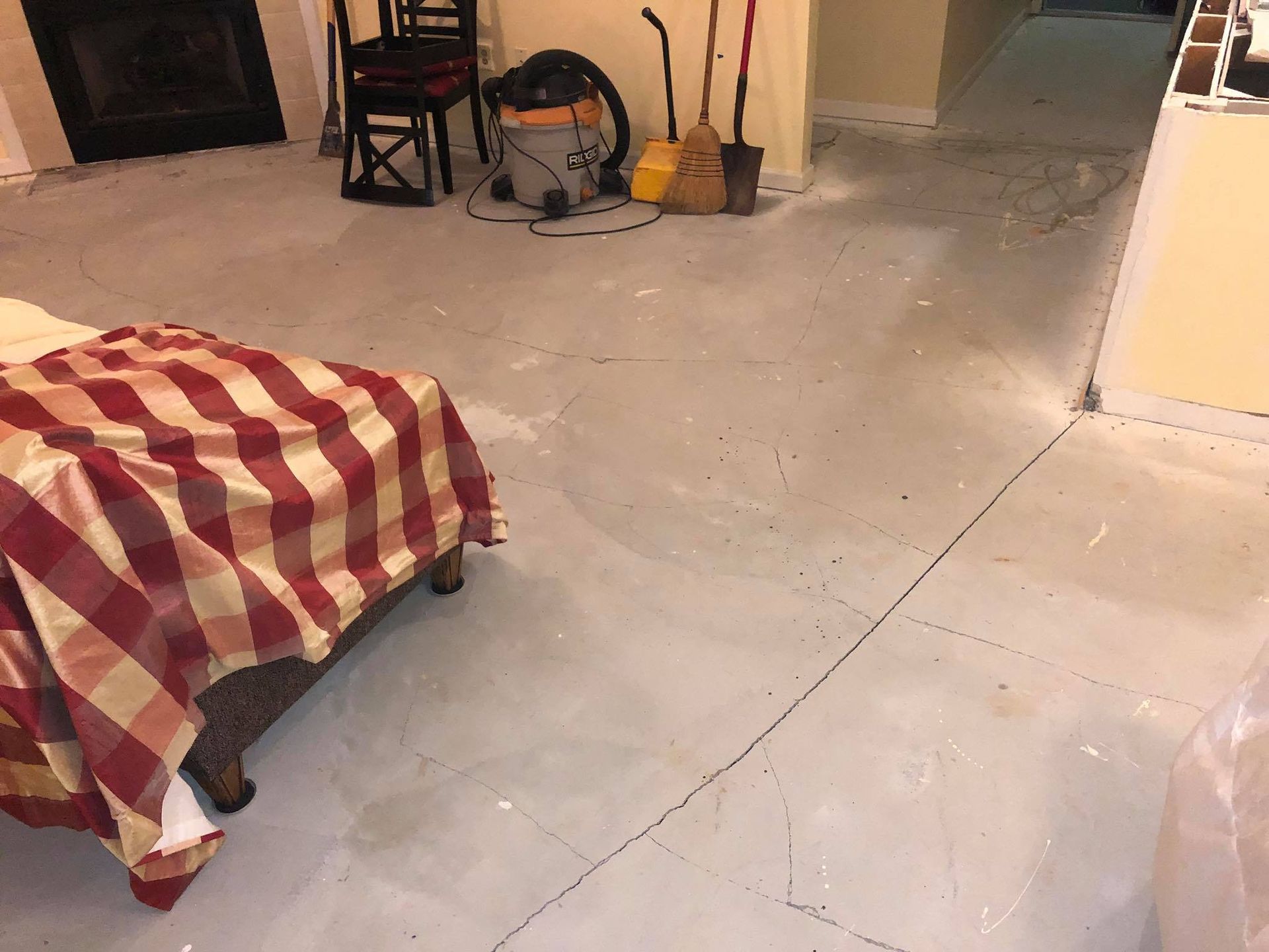 Bedroom with a bed covered by a red and white checkered blanket. Gray cement floor.