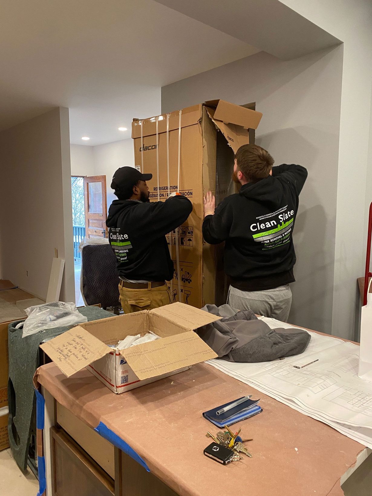 Two movers assembling a large wooden cabinet in a white room with boxes and tools on a table.
