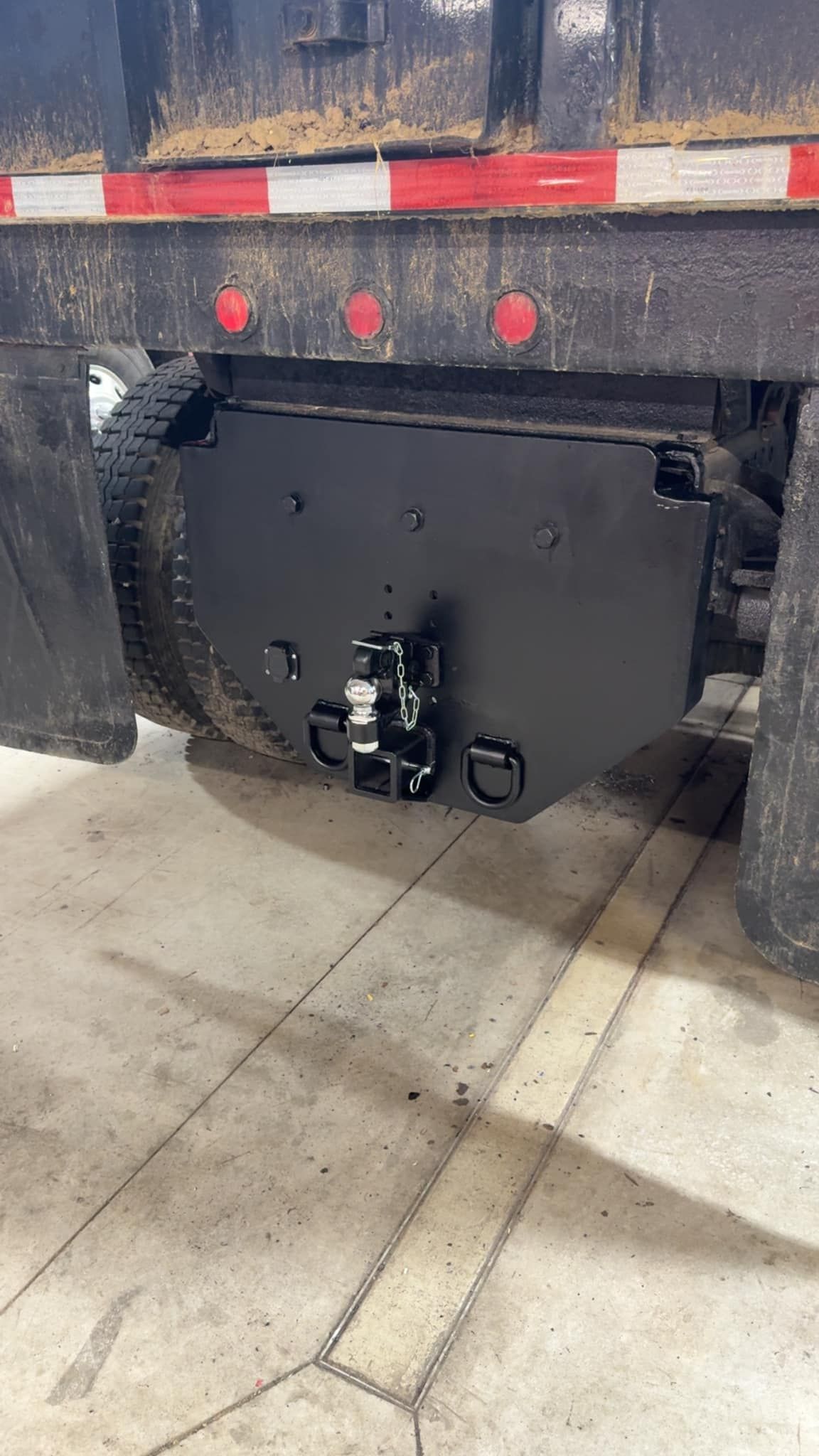 Black truck hitch on the rear of a dump truck, with black painted metal frame and tow rings.
