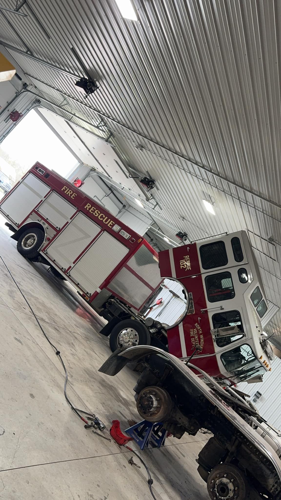 Fire truck and vehicle inside a garage, angled, with metallic ceiling.