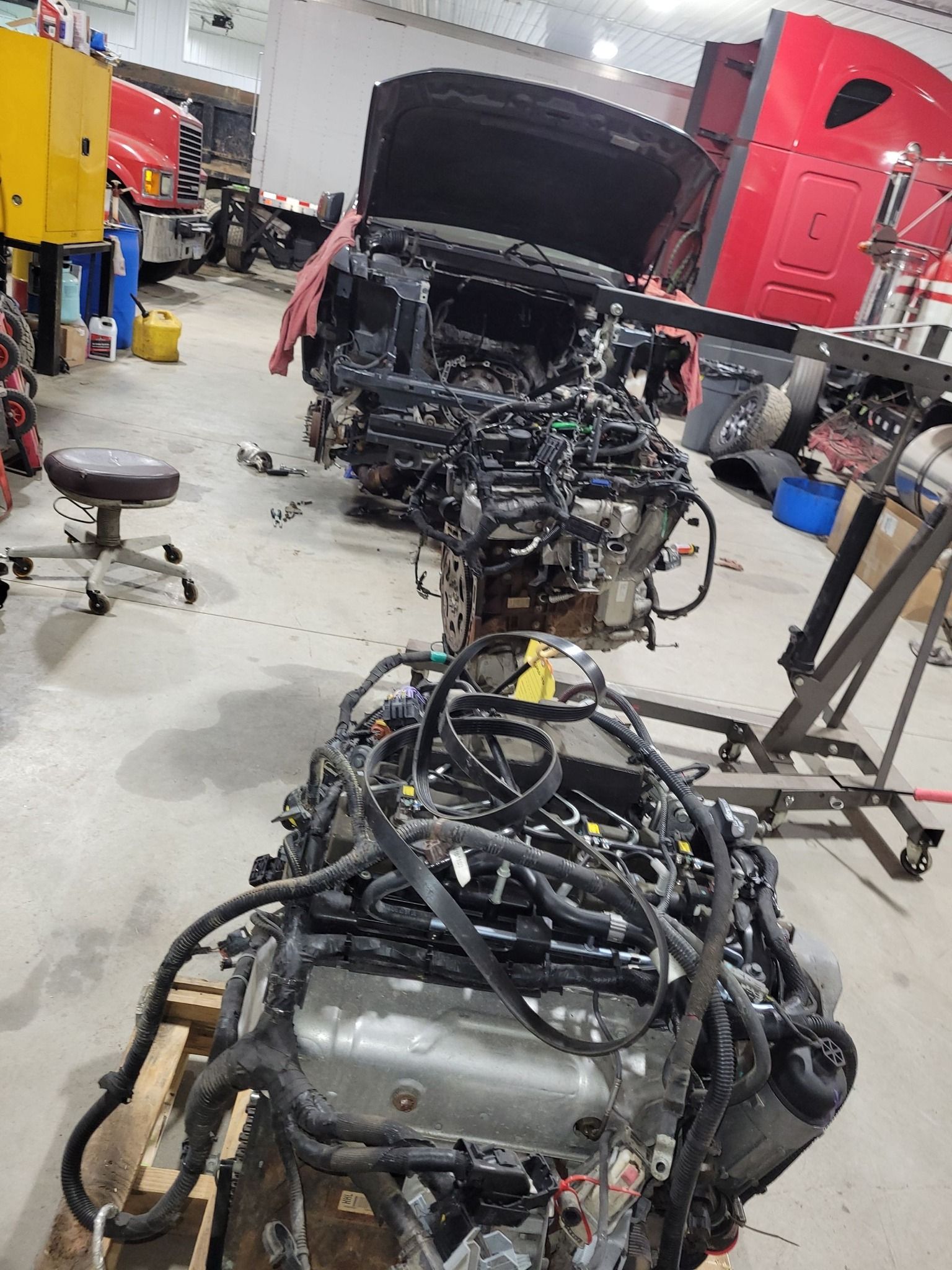Engine and car frame in a repair shop; engine sits on a pallet.