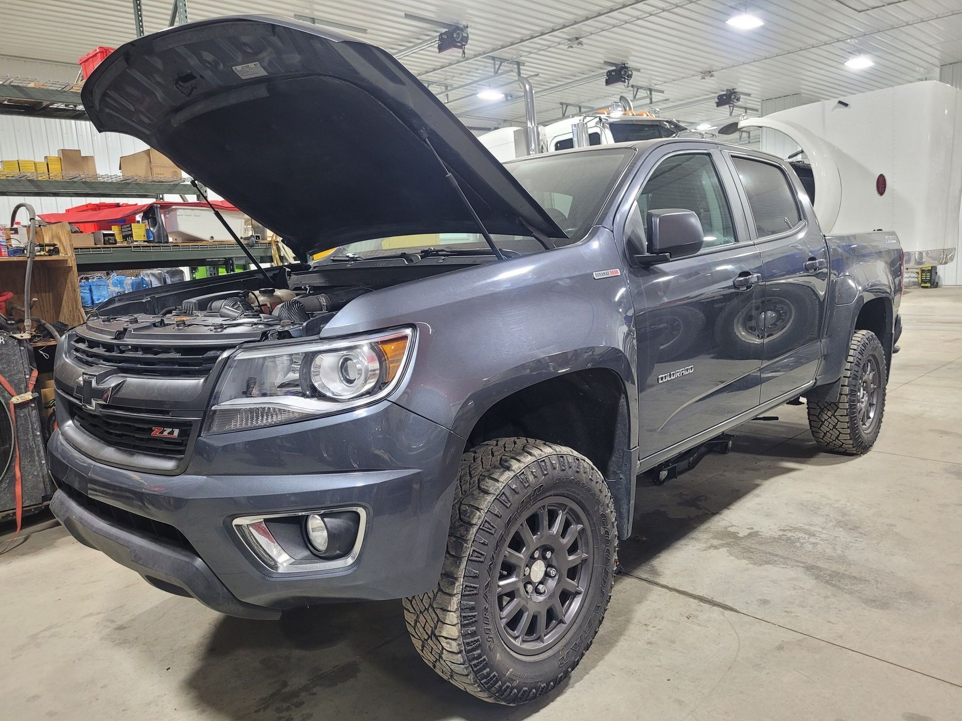 Dark gray Chevrolet Colorado truck with hood open in a garage.