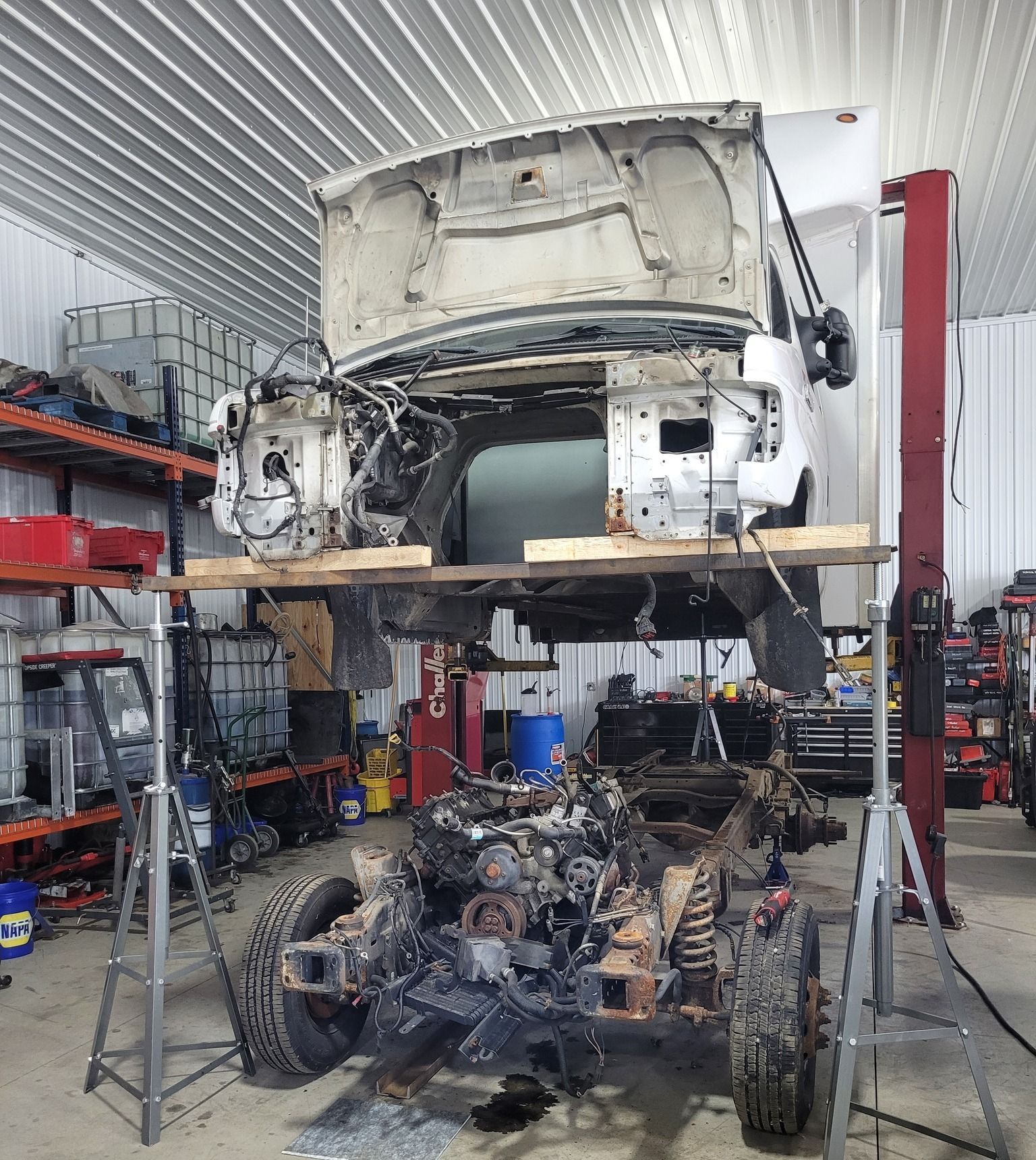 Truck cab separated from frame, supported by wood and jack stands, in a garage.
