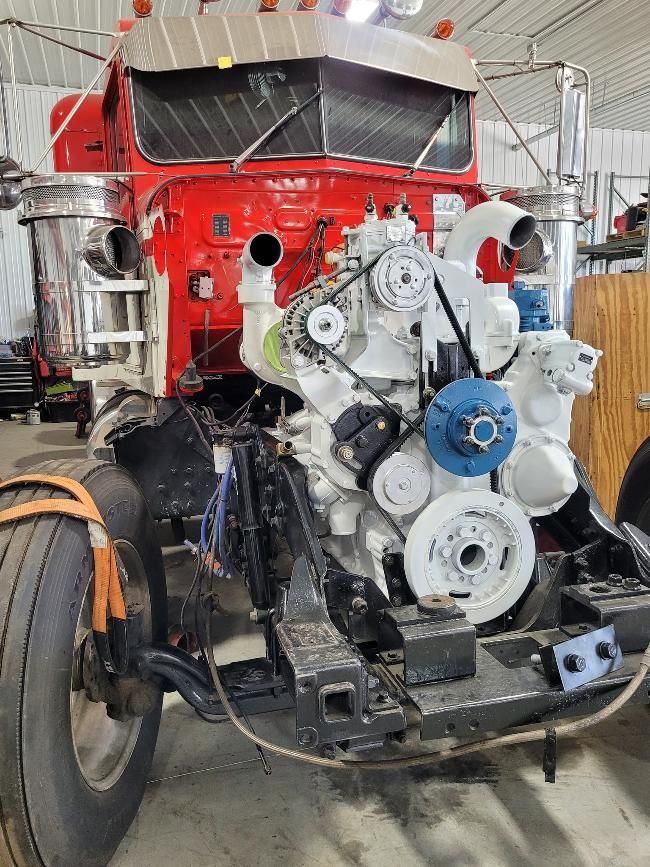 Red semi-truck chassis with a white engine exposed. The truck is inside a garage.