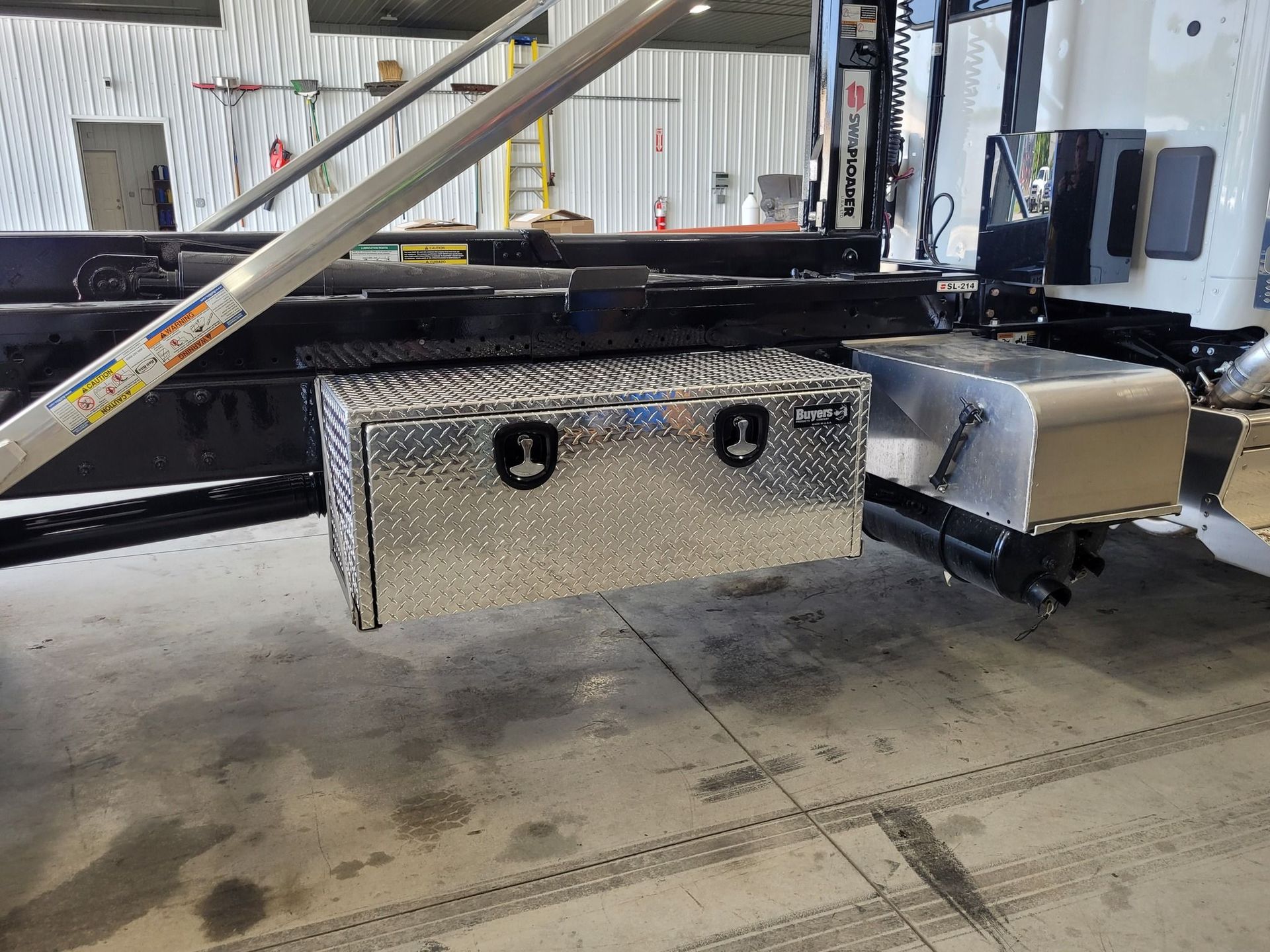 Silver diamond-plated toolbox mounted on a truck frame, with black latches and a reflective finish.