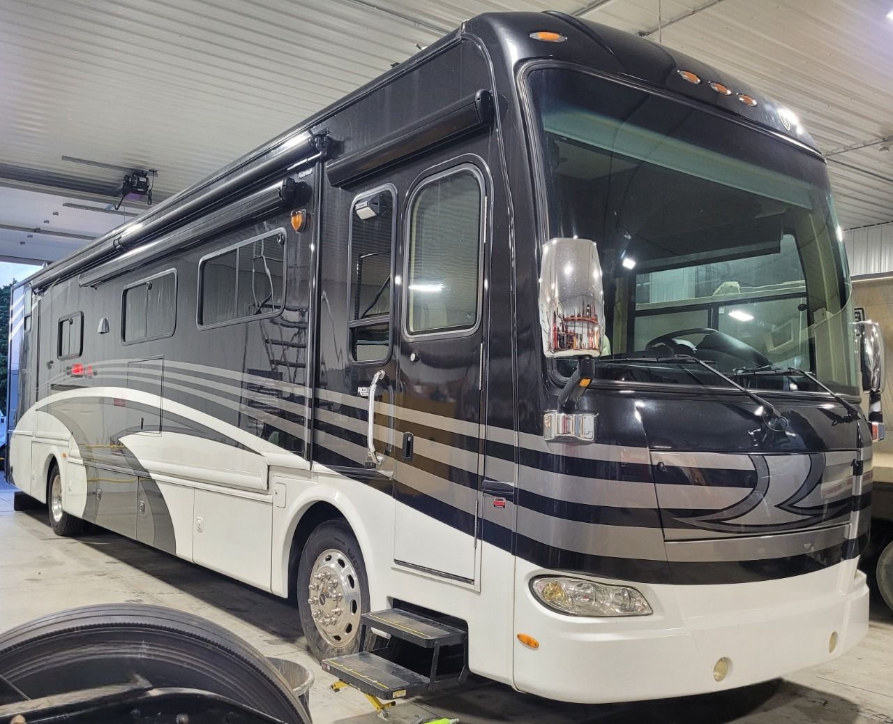 Black and white RV parked inside a garage, silver stripes, large windshield.