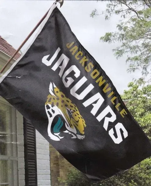Jacksonville Jaguars flag, black background with team logo and text, displayed outdoors.