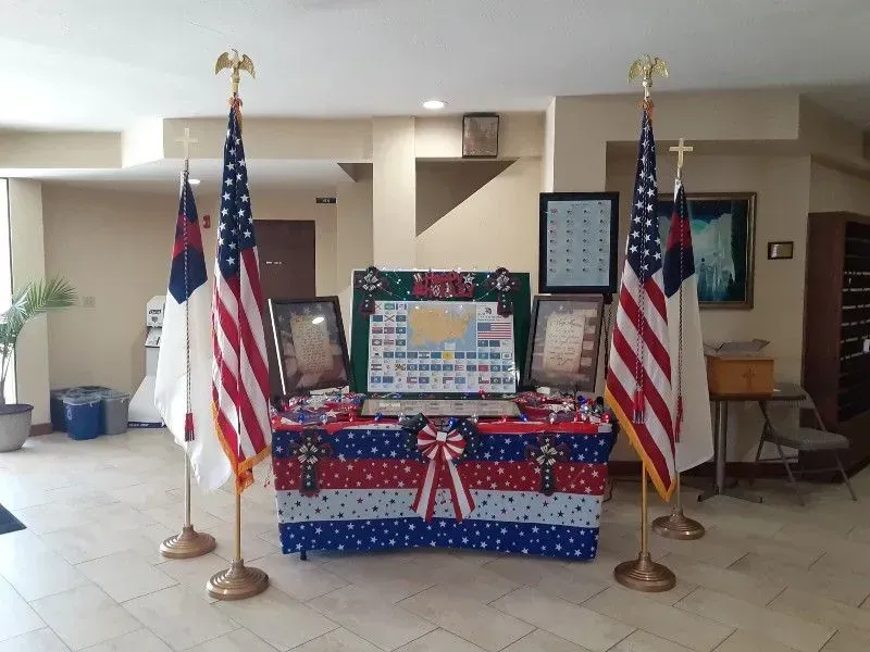 Table display with American flags, Christian flags, framed documents, and a map, indoors.