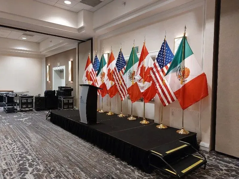 Flags of Canada, USA, and Mexico line a stage with a podium in an event room.