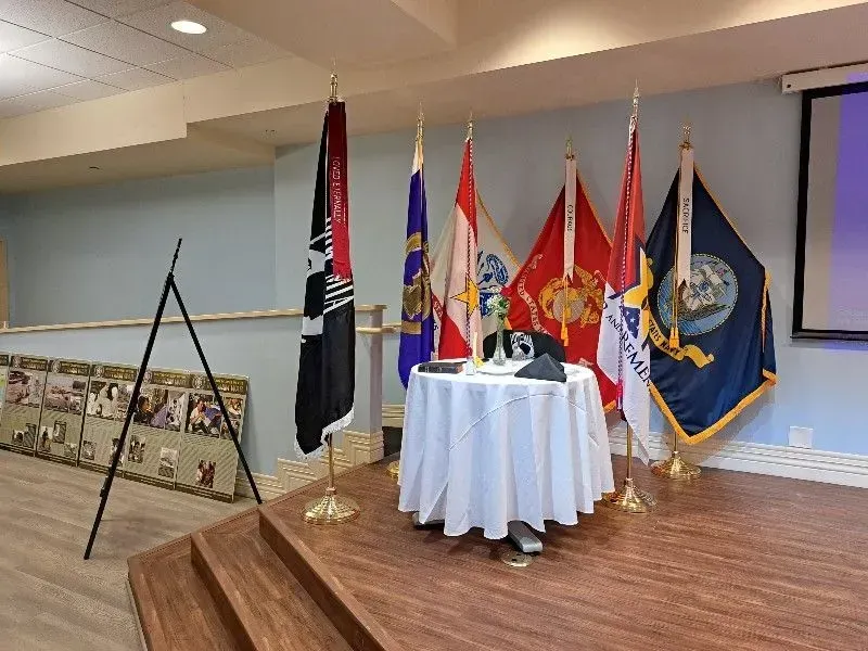 Flags and memorial table on a stage; the flags represent various military branches.