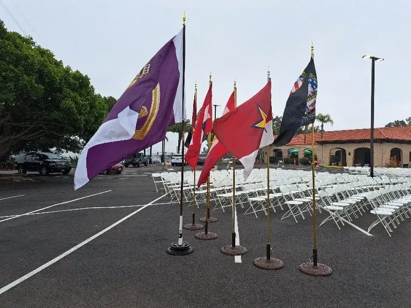 Flags on poles in a parking lot, with rows of white chairs.