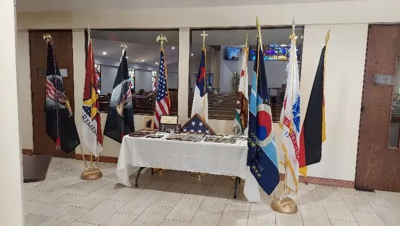 Flags and memorial display. Table with folded flag, medals, and US, state, and military flags.