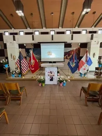 Ceremony inside a church. Flags, screen, photo display; chairs in front.