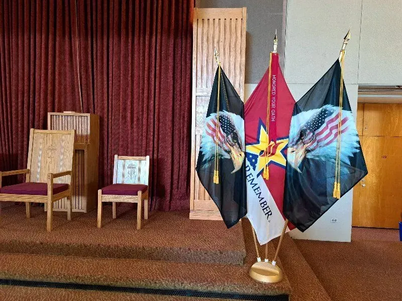 Flags with eagles, memorial display with chairs, red curtains, wooden cabinets.