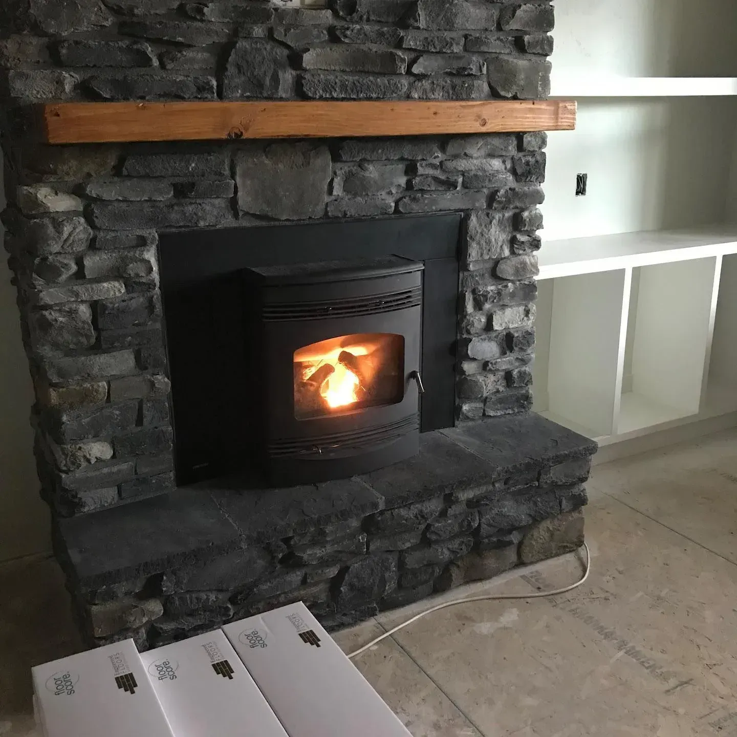 Fireplace with stone surround, wood mantle, and pellet stove burning inside. Shelves to the right.
