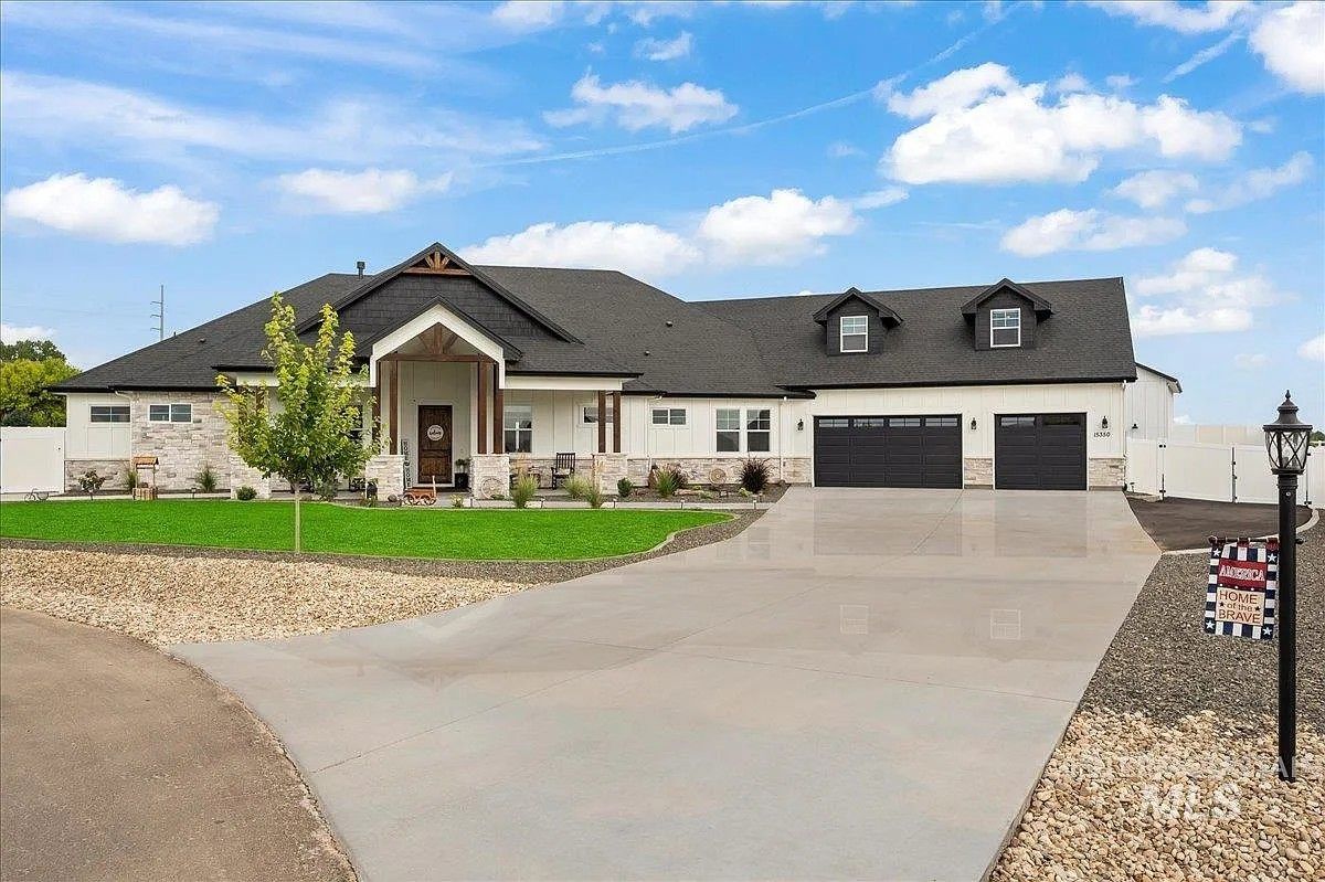 A modern, white house with a dark roof and a long concrete driveway under a blue sky.
