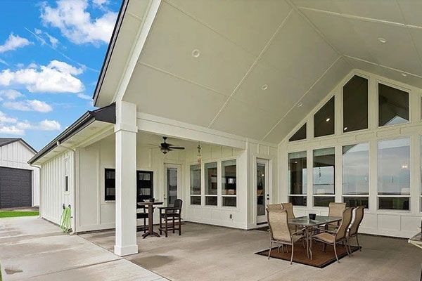 Covered patio with dining set and bar stools, white walls, and glass windows.