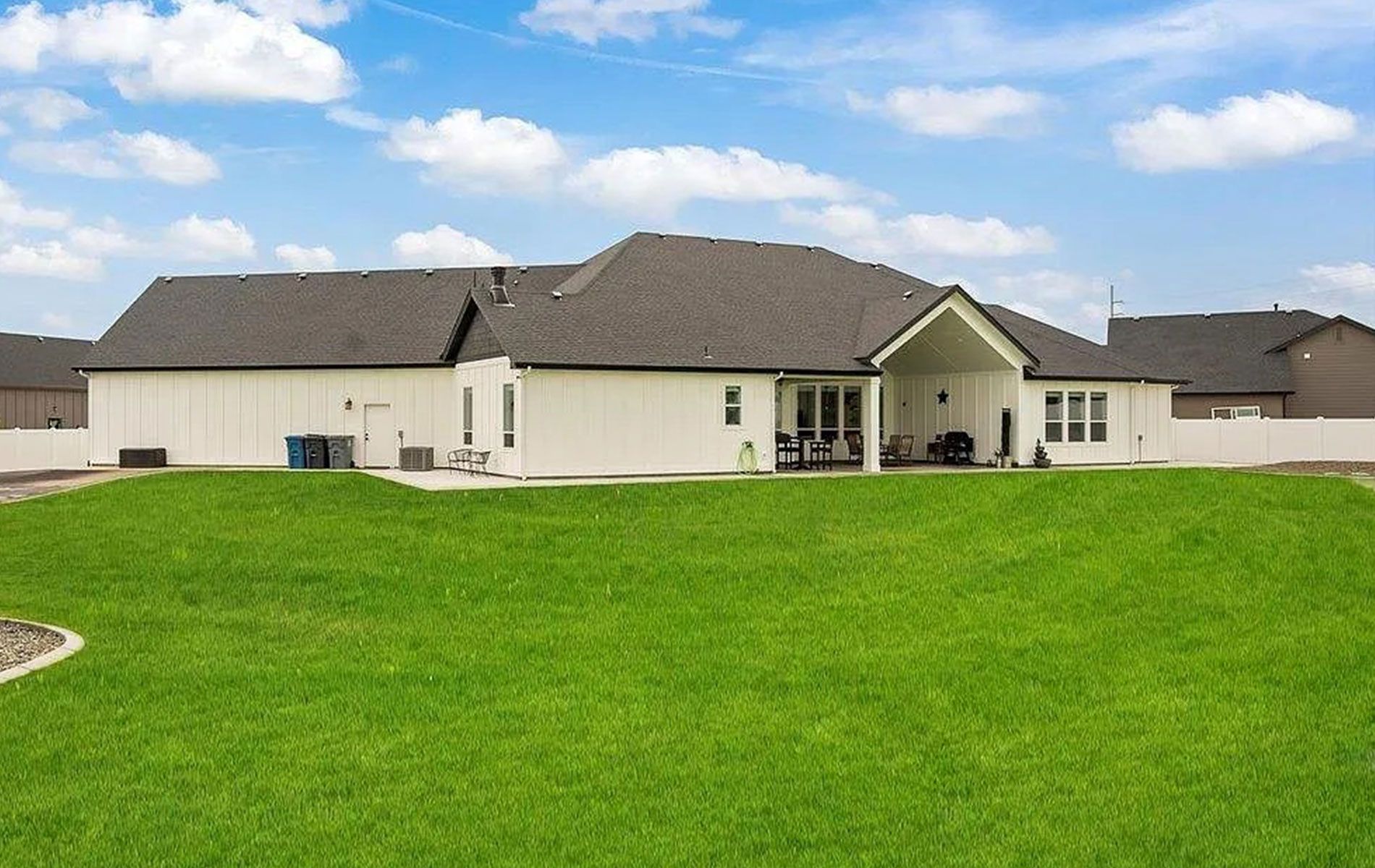White house with black roof, large green lawn, blue sky with clouds.