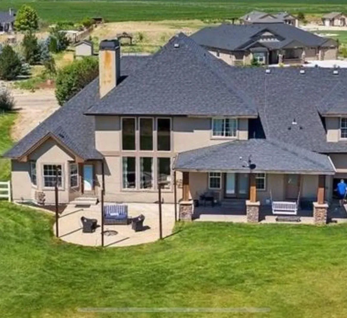 Large two-story house with a dark gray roof and multiple patios on a grassy lawn.