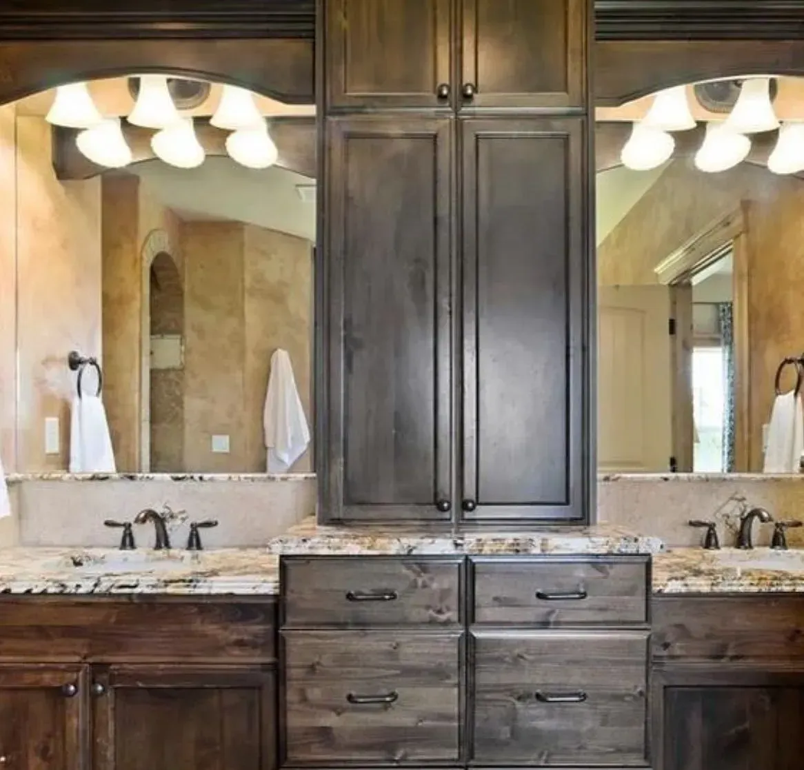 Bathroom vanity with brown cabinetry, granite countertops, mirrors, and lighting.