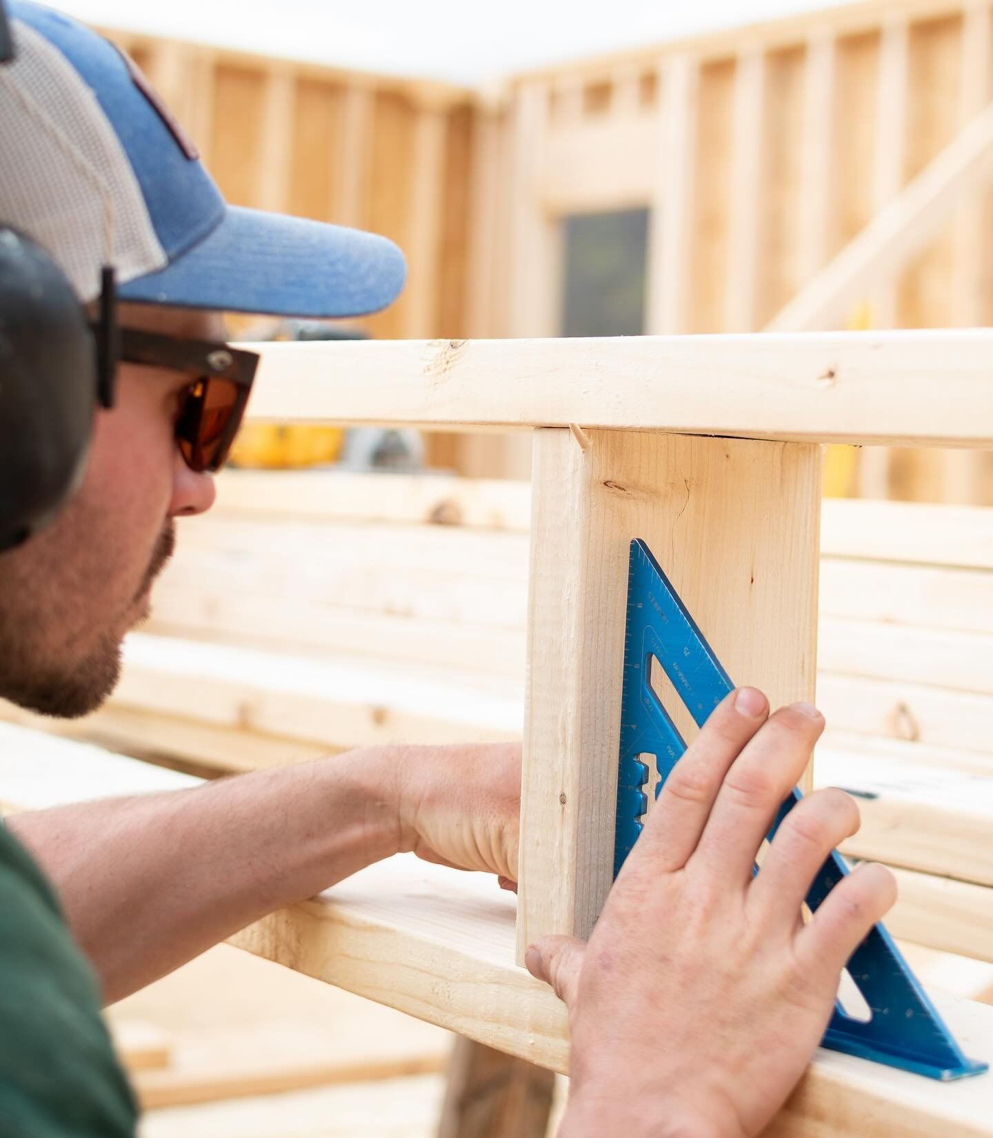 A man is using a blue triangle to measure a piece of wood.