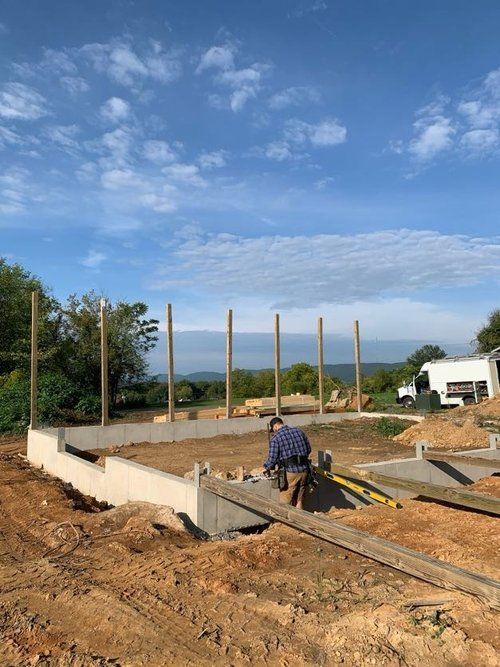 A man is standing in the dirt in front of a building under construction.