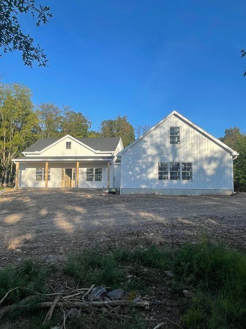 A large white house is being built in the middle of a dirt field.
