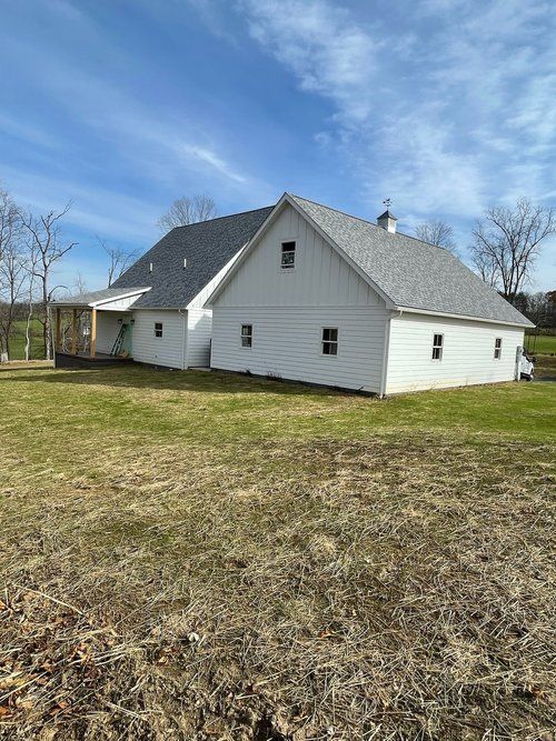 A white house with a gray roof is sitting in the middle of a grassy field.