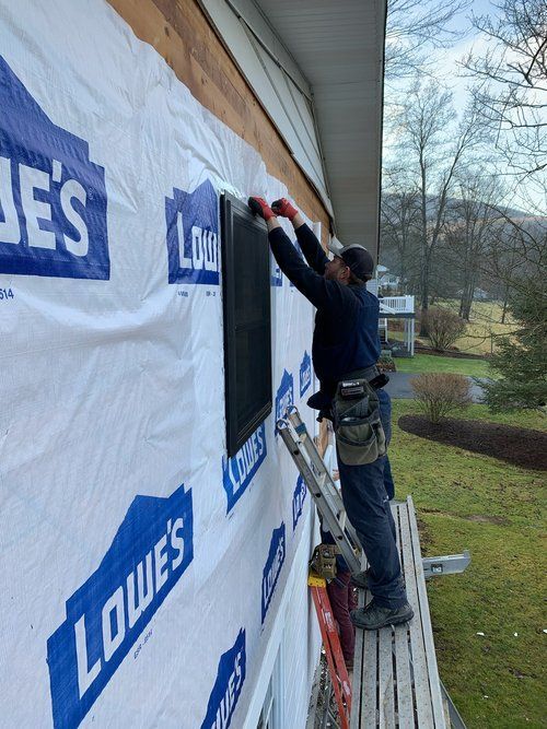 A man on a ladder is installing a screen on the side of a house.