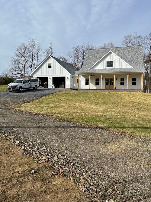 A white house with a gray roof is sitting on top of a lush green field.