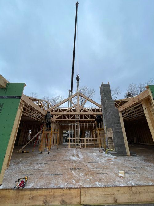 A crane is lifting a truss on top of a house under construction.