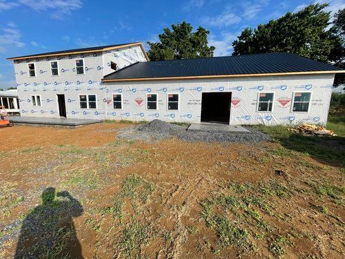 A large white house with a black roof is being built in a dirt field.