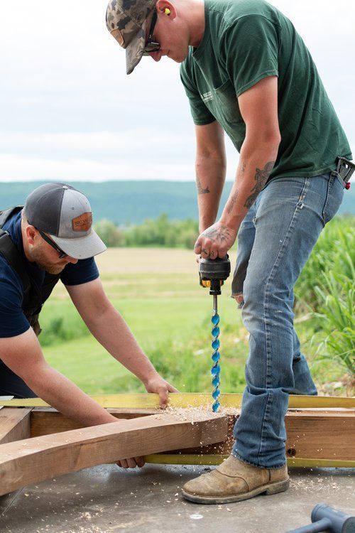 Two men are working on a piece of wood with a drill.