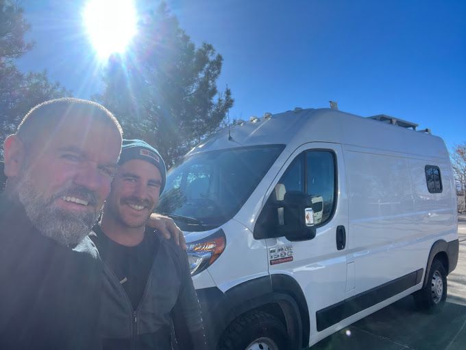 two men are posing for a picture in front of a white van