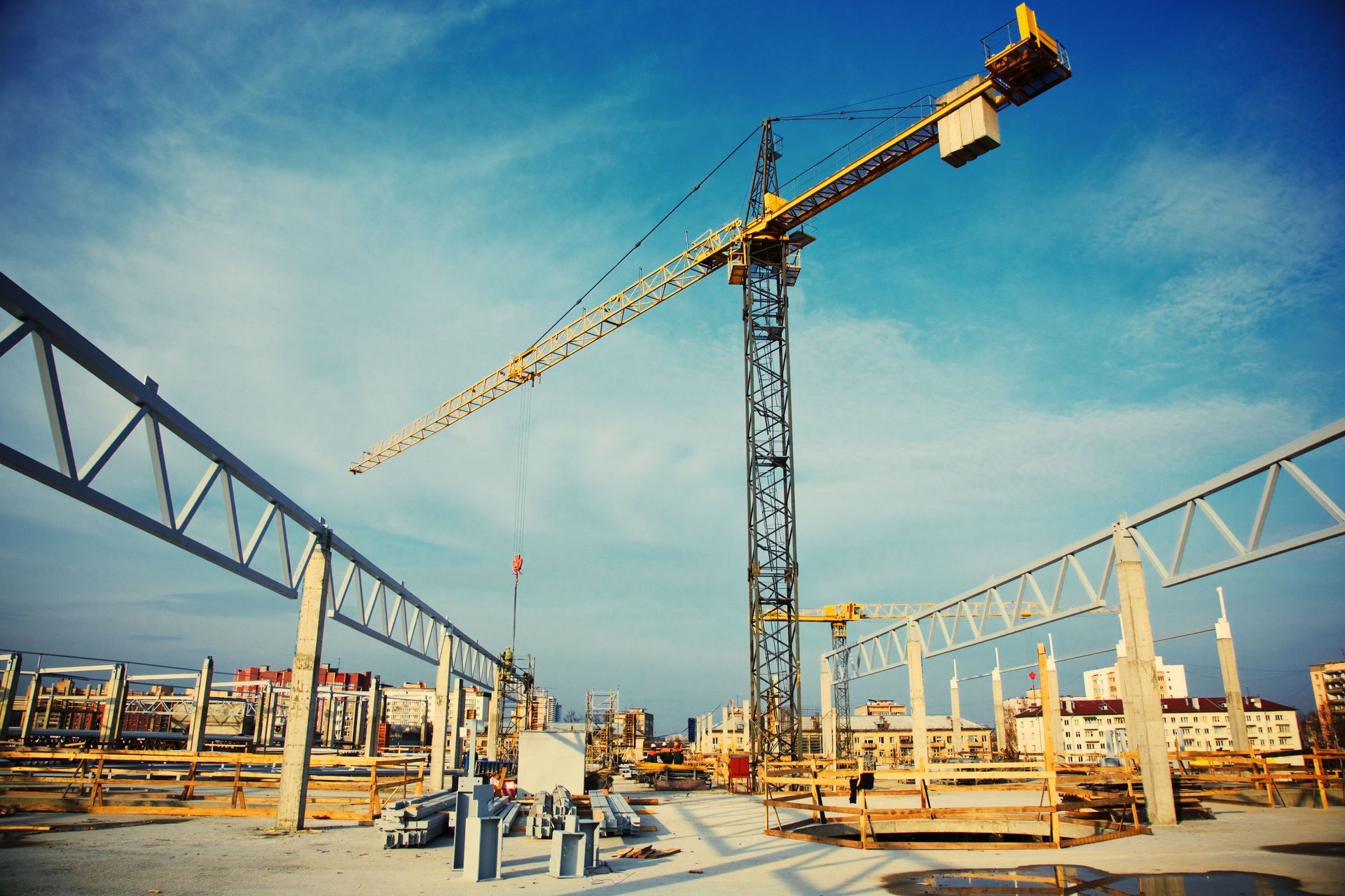 Construction site with a yellow crane under a blue sky, with building framework in the foreground.