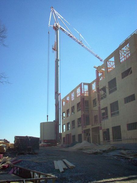 Construction site with crane lifting materials to a multi-story wooden building against a blue sky.