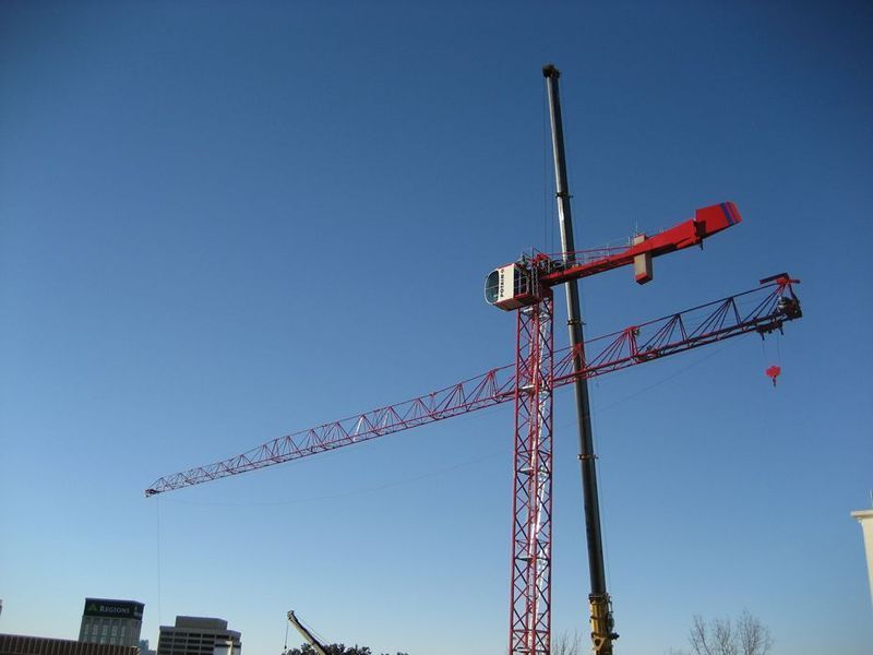 Red construction crane against a clear blue sky, with a long horizontal arm and a vertical tower.