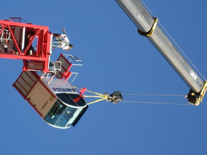 A crane lifting a construction crane cab against a clear blue sky.