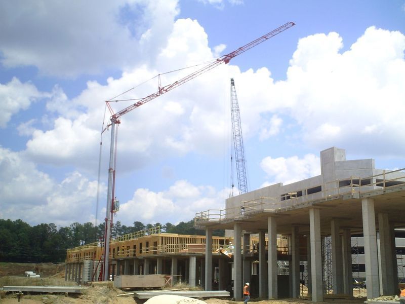 Construction site with tall cranes building a concrete structure under a partly cloudy sky.